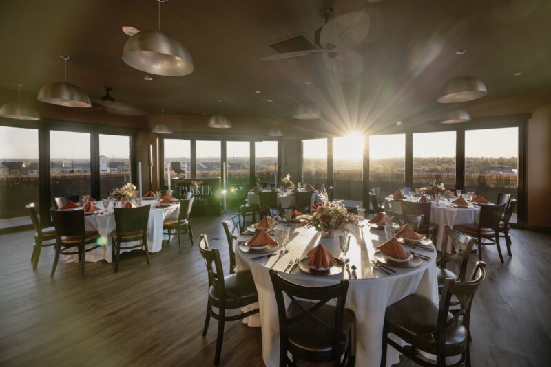 A banquet room set up with round tables and white linens, orange napkins.