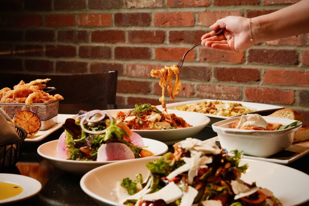 Pasta being twirled on a fork, surrounded by assorted salads and sides from Ovest Via.